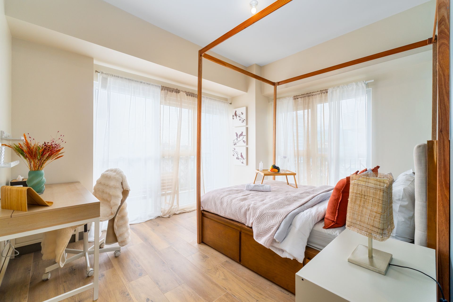 Four poster bed in a bright room with desk, bedside table and curtains