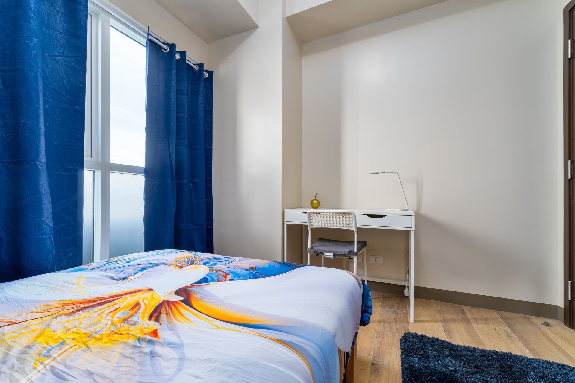 A bedroom with a bed , desk , and blue curtains.