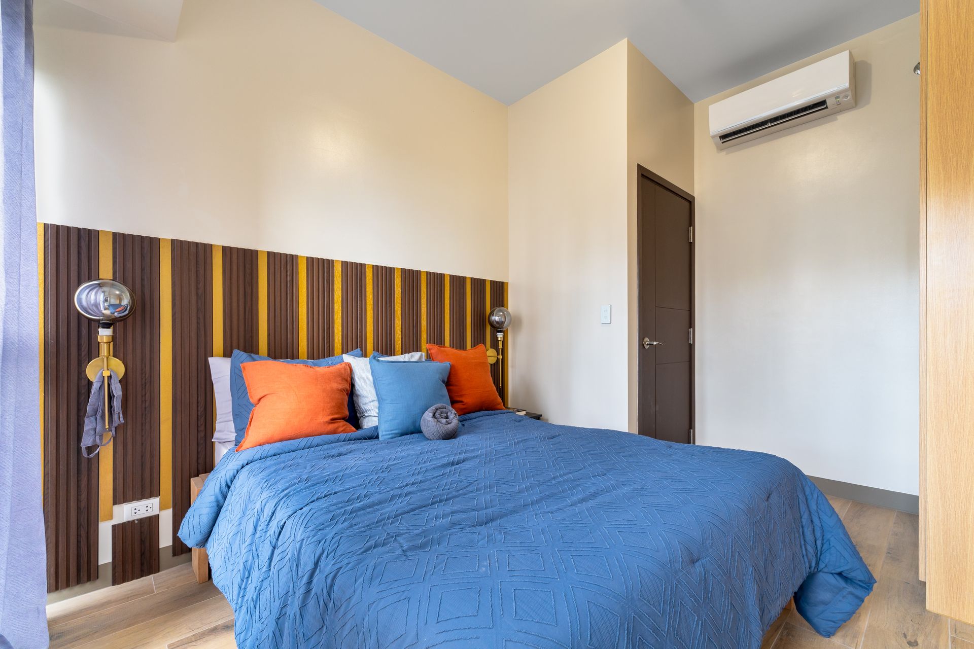 Bed with blue cover, pillows in blue and orange and a feature wall