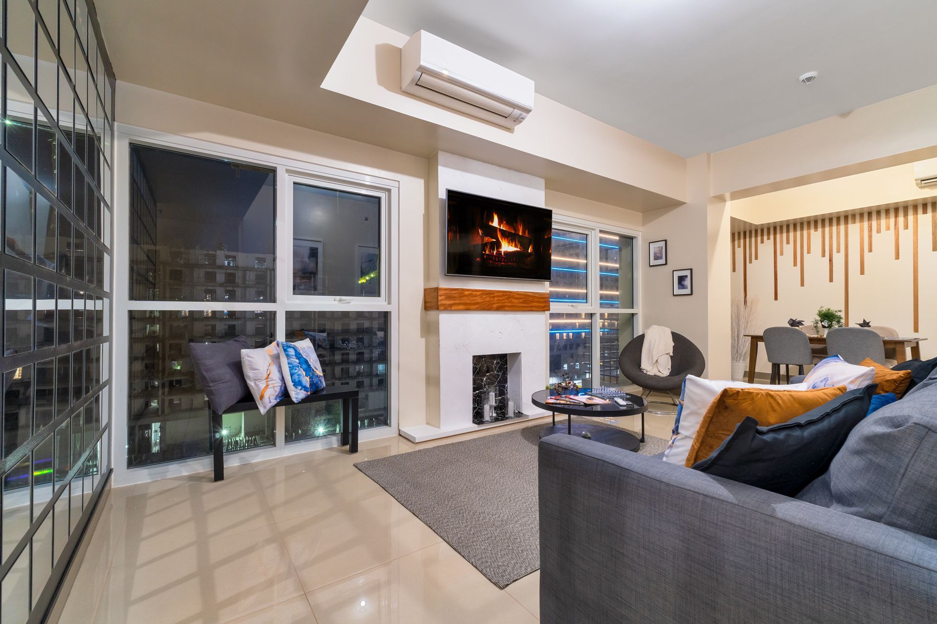 Living area with gray sofa, bench chair, faux fireplace and TV