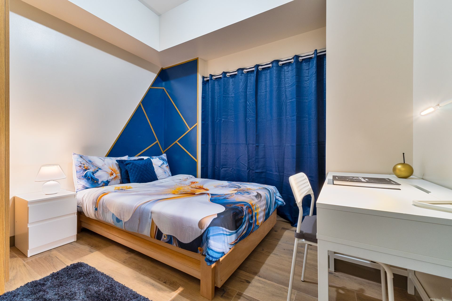 A bedroom with a bed , desk , nightstand and blue curtains. Captains Quarters at Bayshore Luxe by Prime, Manila