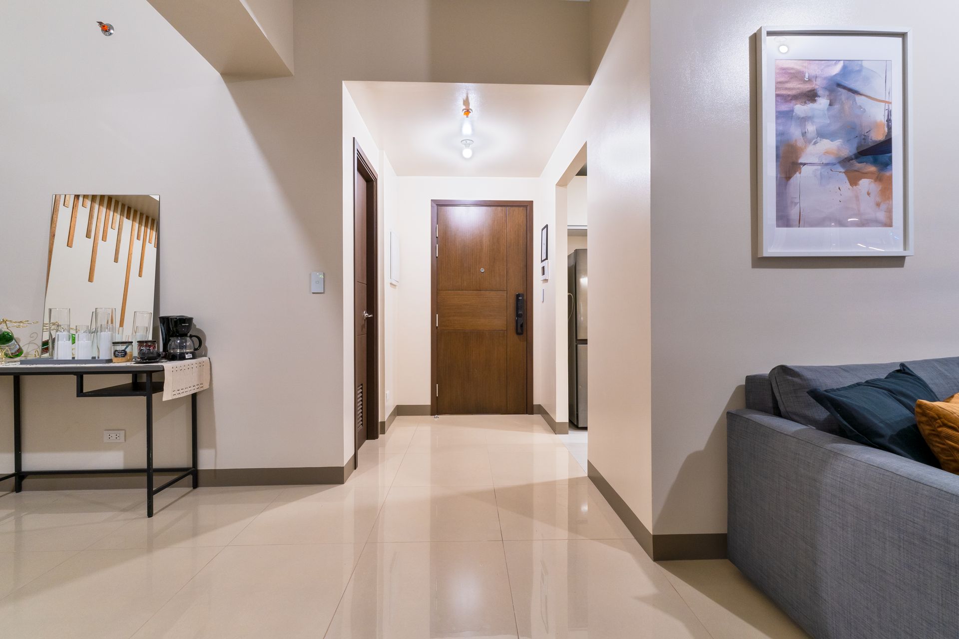 A living room with a couch , table , mirror and door. Captains Quarters at Bayshore Luxe by Prime, Manila