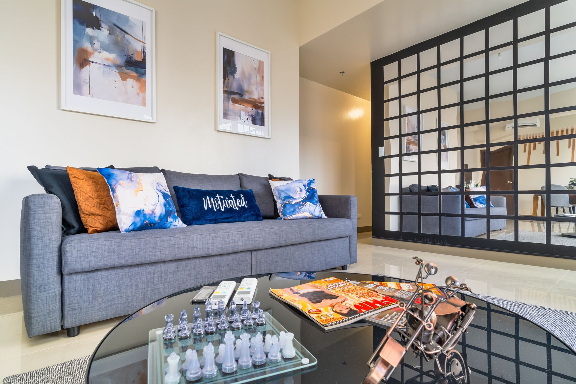 Gray sofa with cushions in blues and oranges, crystal chess set on a glass table