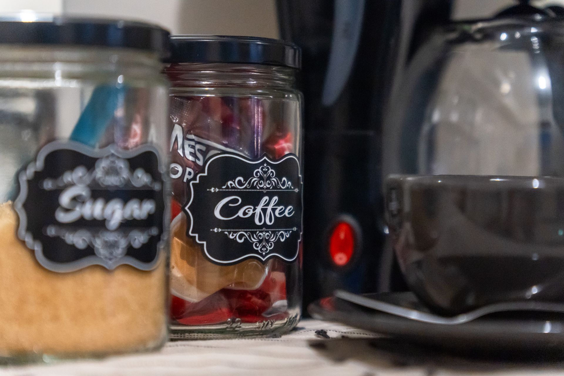 A jar of sugar and a jar of coffee are on a counter next to a coffee maker.