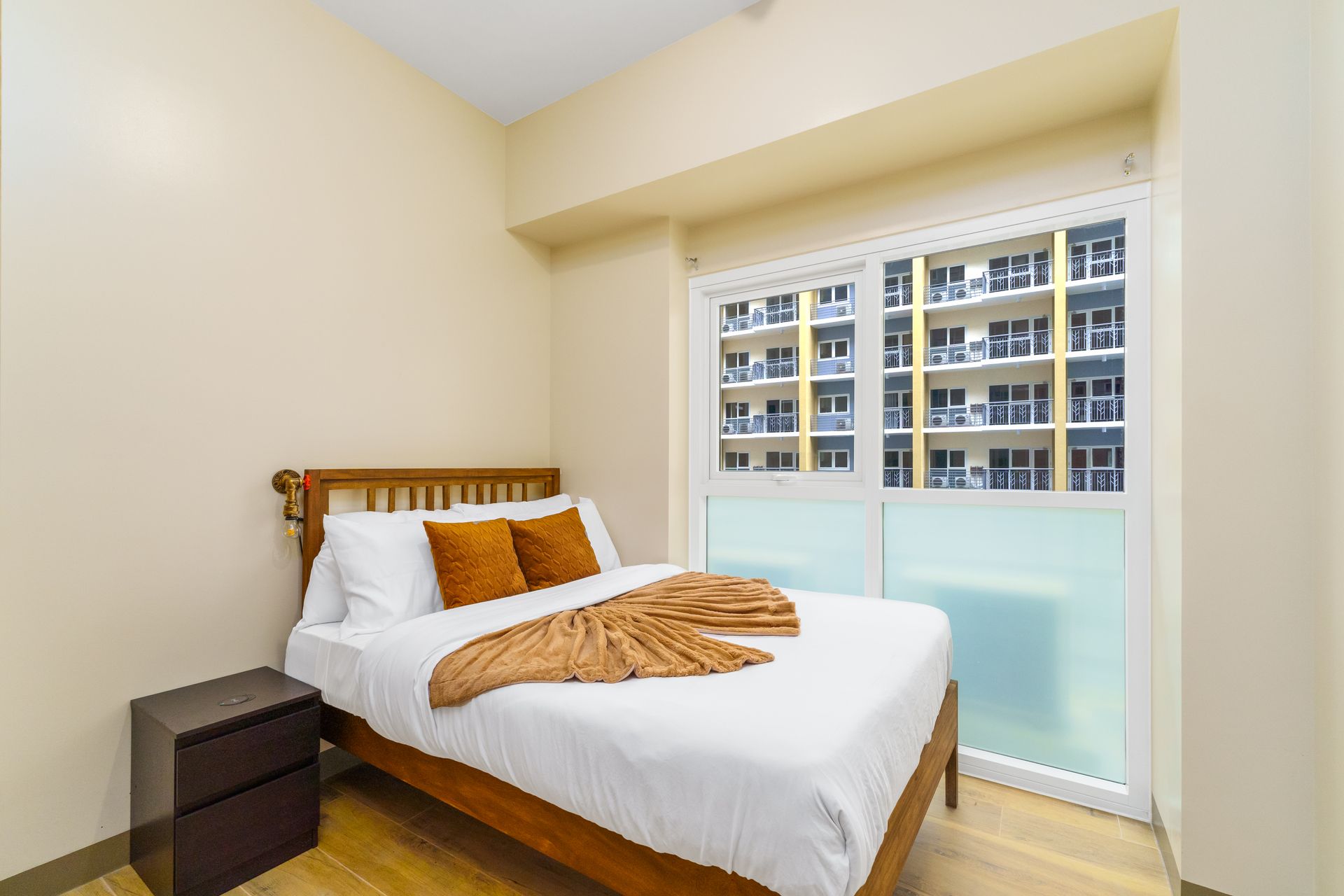 Wooden Bed with white linens and rust brown cushions and throw