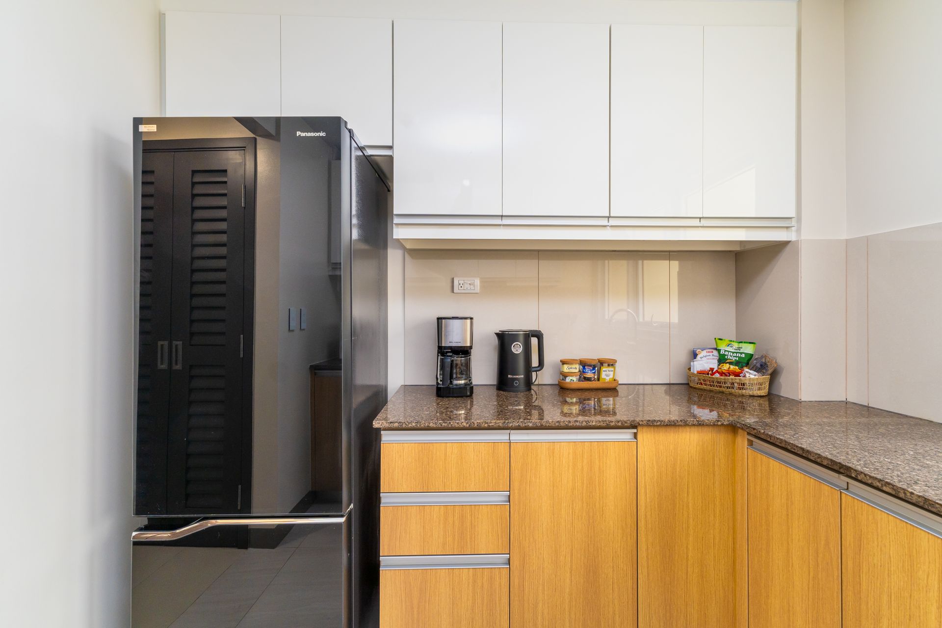 kitchen counterspace with a coffee maker and kettle, a tall fridge to the left and cupboards above