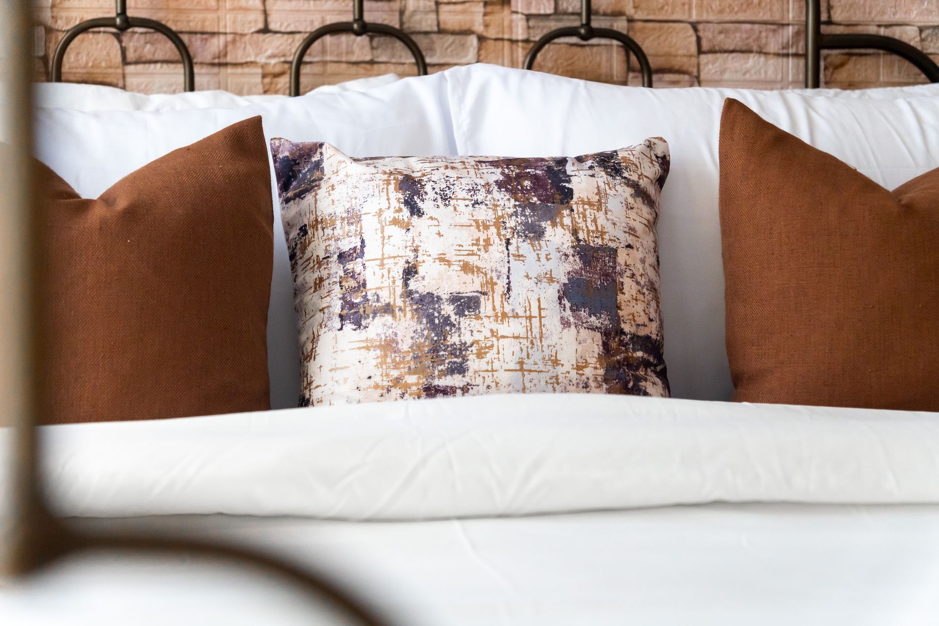 Wrought iron Bed frame, bed with white pillows and linens, and rust brown cushions