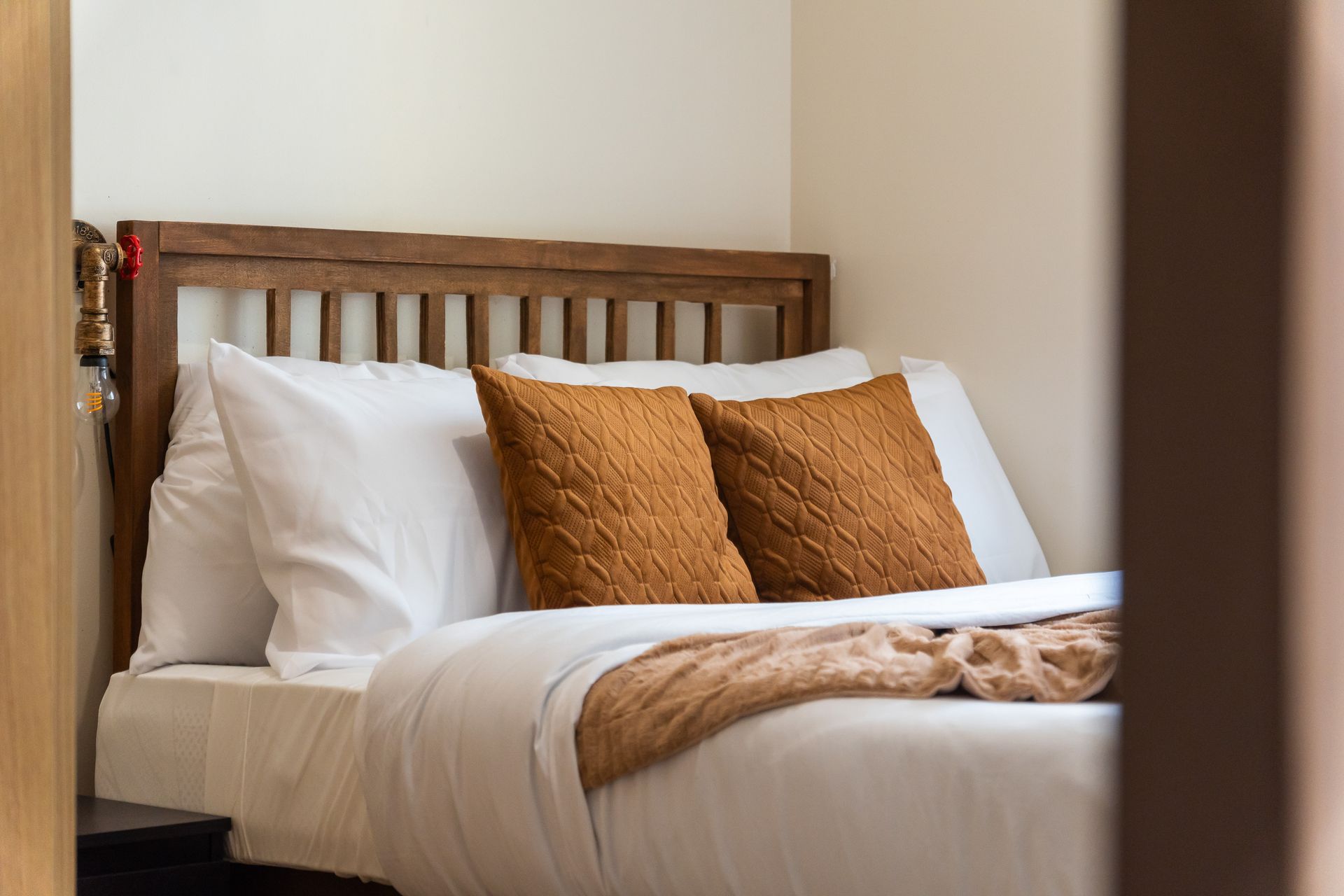Wooden Bed with white linens and rust brown cushions and throw