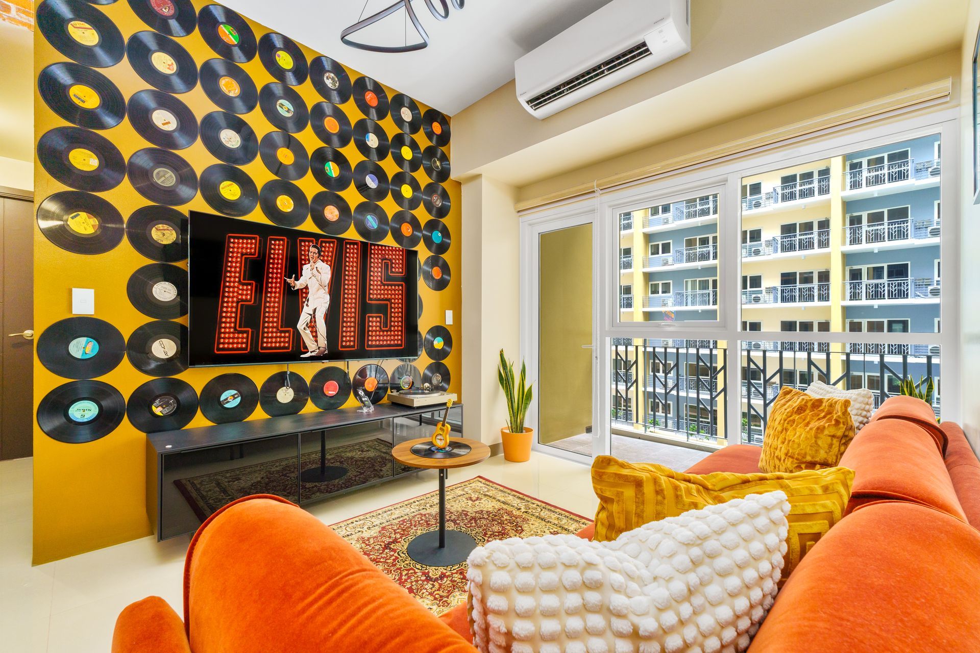 Vibrant living room with orange velvet sofa, Rug and a wall decorated with old vinyl records with a flatscreen TV