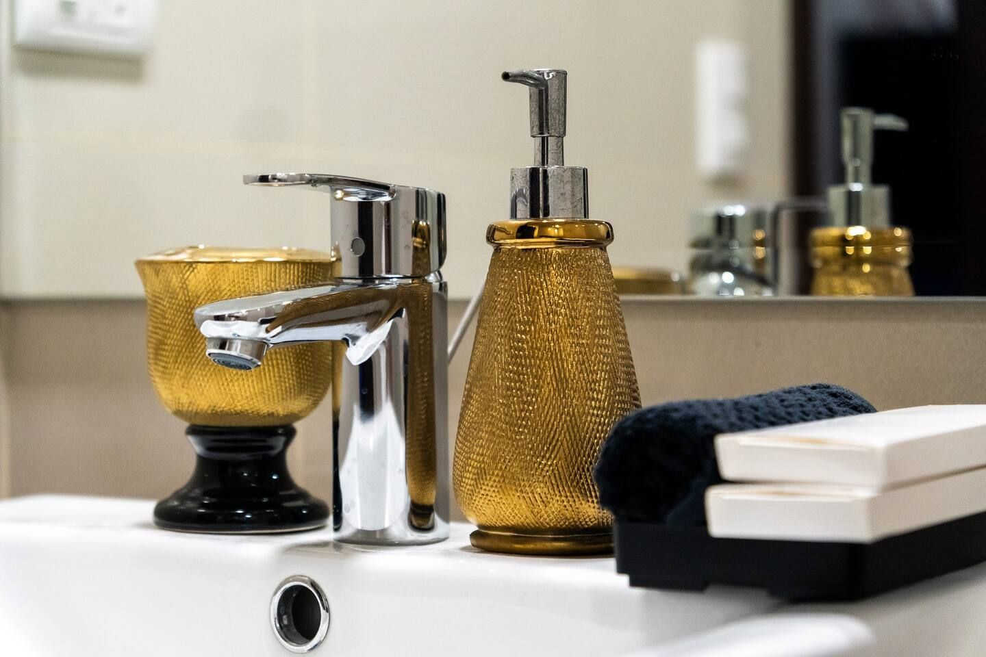 A bathroom sink with a faucet , soap dispenser , and towels.   The Den at Bayshore Luxe by Prime, Manila
