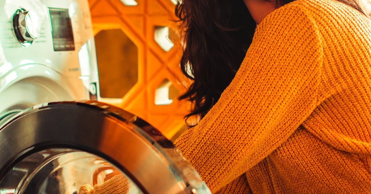 A woman in a yellow sweater is sitting in front of a washing machine.