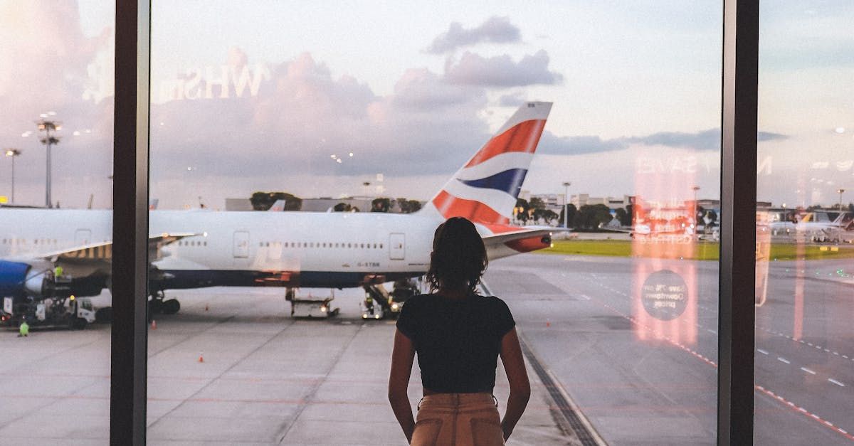 A woman is standing in front of a window at an airport looking out at an airplane.