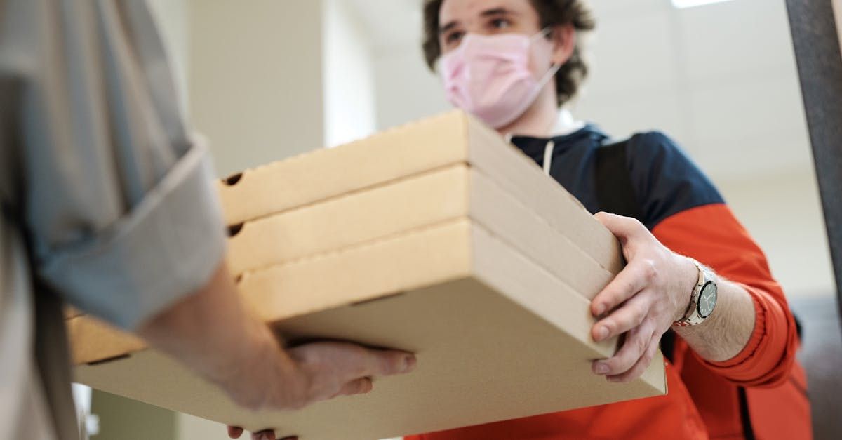 A man wearing a mask is holding a box of pizza.