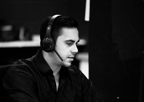 A man wearing headphones and a microphone is sitting in front of a computer.