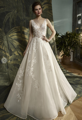 Woman in a white lace wedding gown, standing outdoors with a blurred pink background.