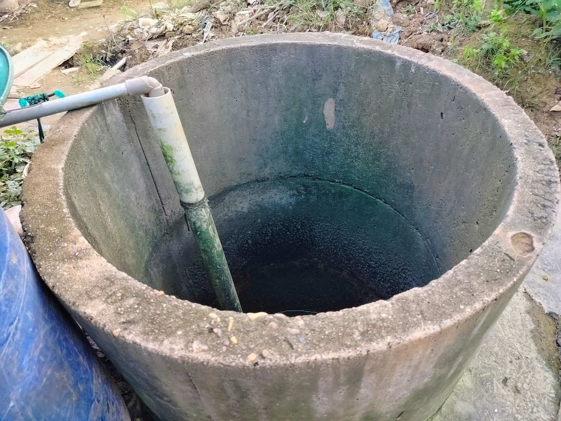 A mossy concrete water well with PVC pipe in an outdoor area.