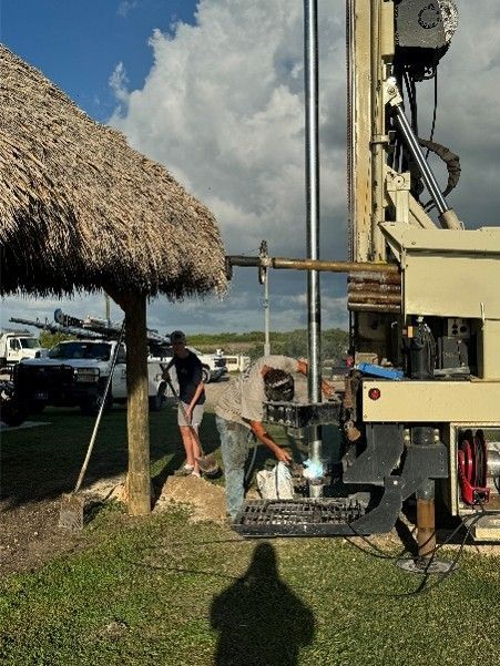 two workers operating a drilling rig on grassy land.