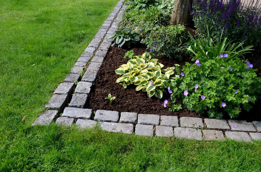 A garden with a brick border and flowers in the corner
