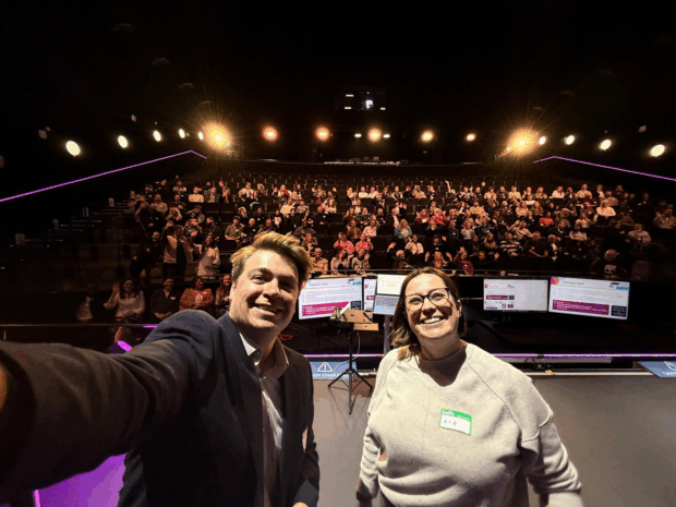 Sam Nutt and Liz Adams from GDS Local on stage with 150 Local Government Innovation Hackathon participants in the background. 

