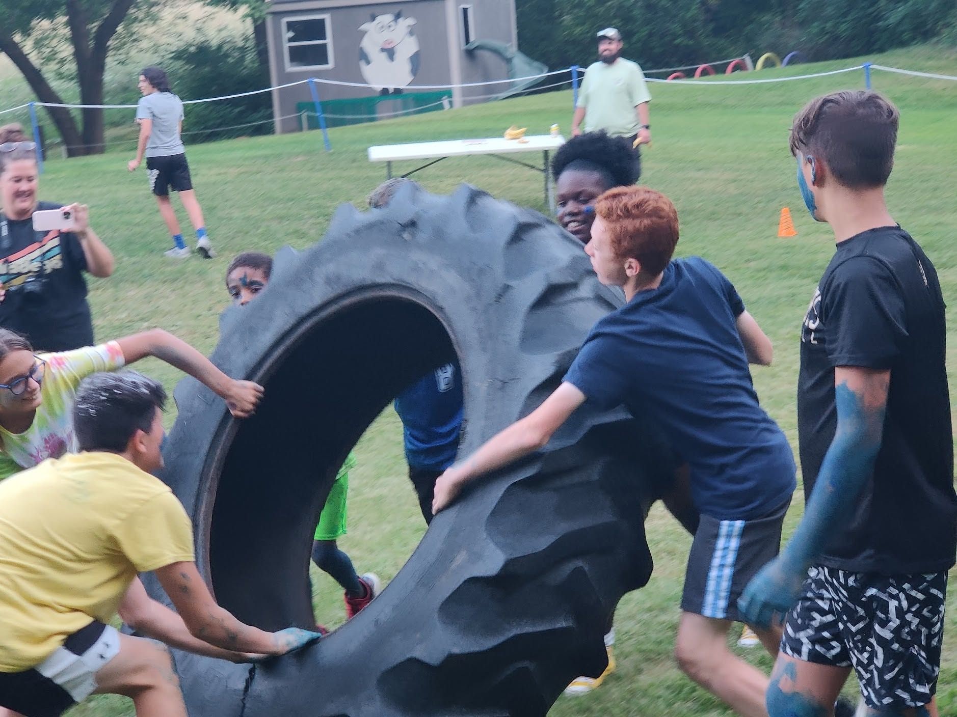 People pushing a large tire on a grassy field during an outdoor activity.