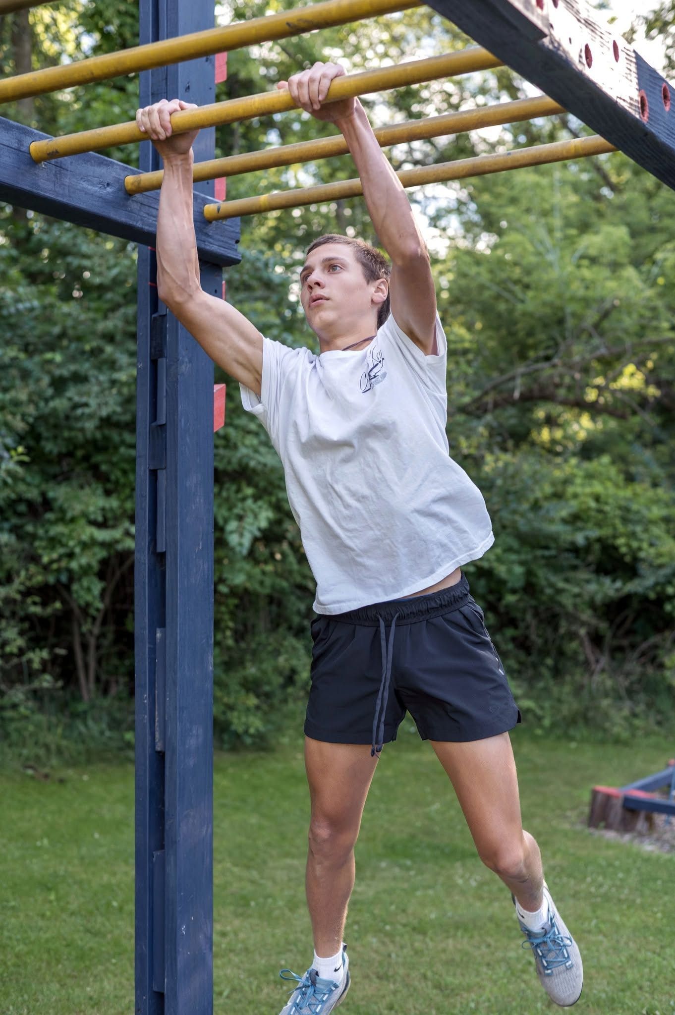 Person hanging from yellow monkey bars in a grassy outdoor park.