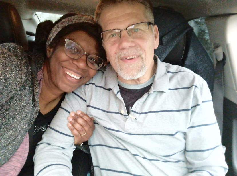Two smiling people seated in a car, leaning close together and taking a selfie.