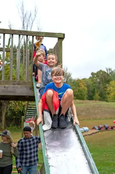 Children sitting on a playground slide, one smiling at the bottom while others wait above outdoors