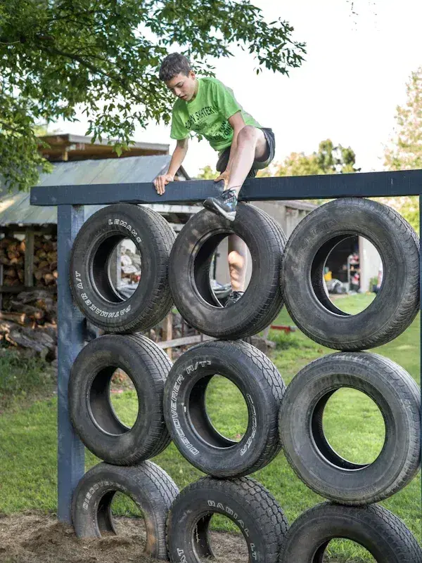 Person climbing over a wall made of stacked tires outdoors