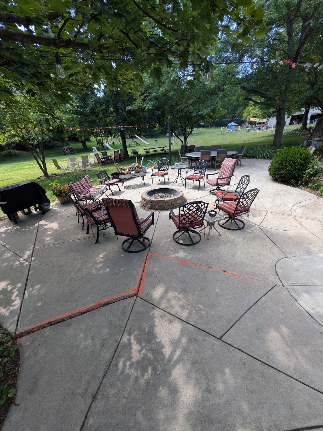 Outdoor patio with red chairs around a fire pit under trees in a park