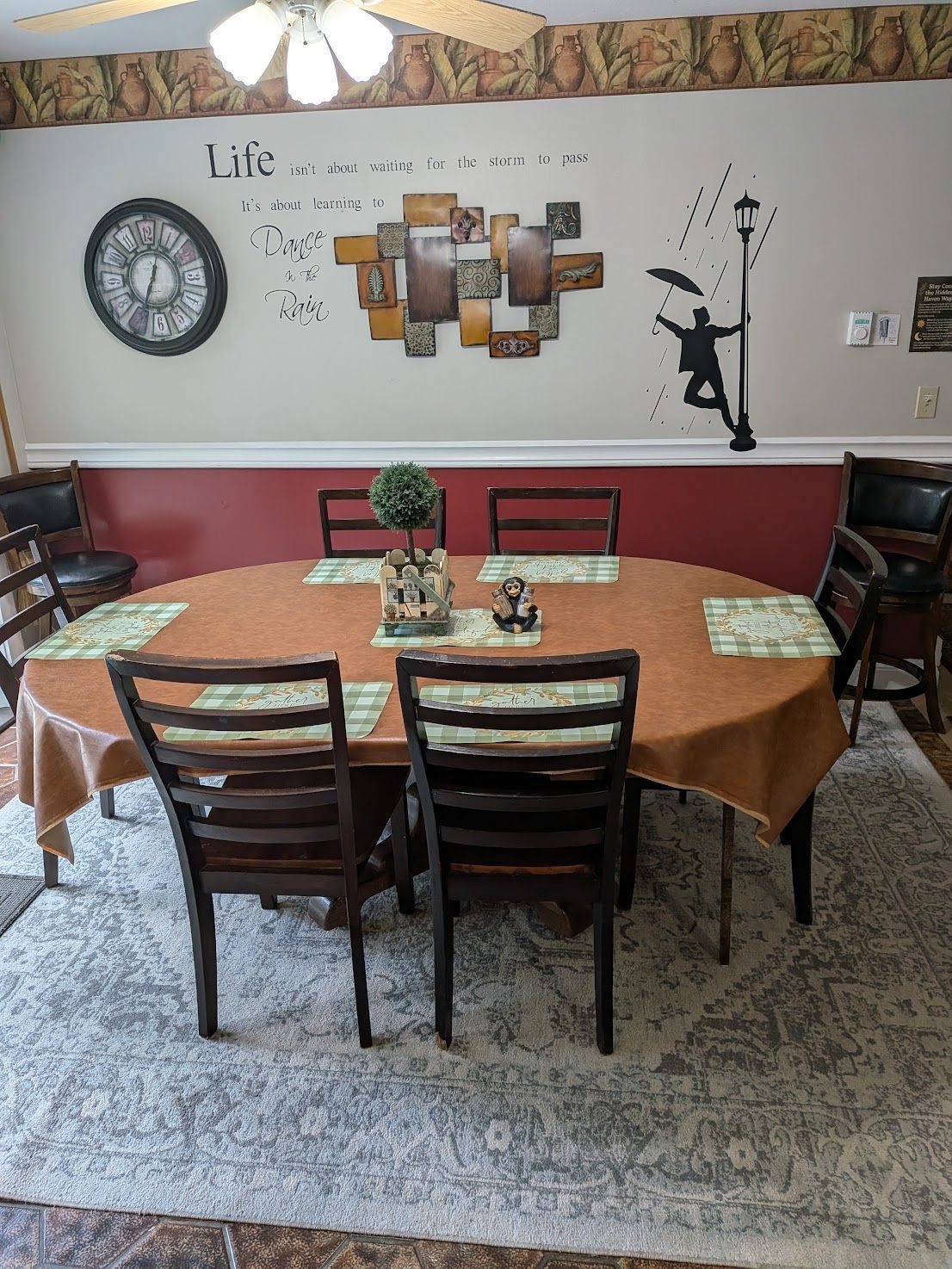 Dining room with round table, four chairs, wall art, and a clock on a white-and-maroon wall.