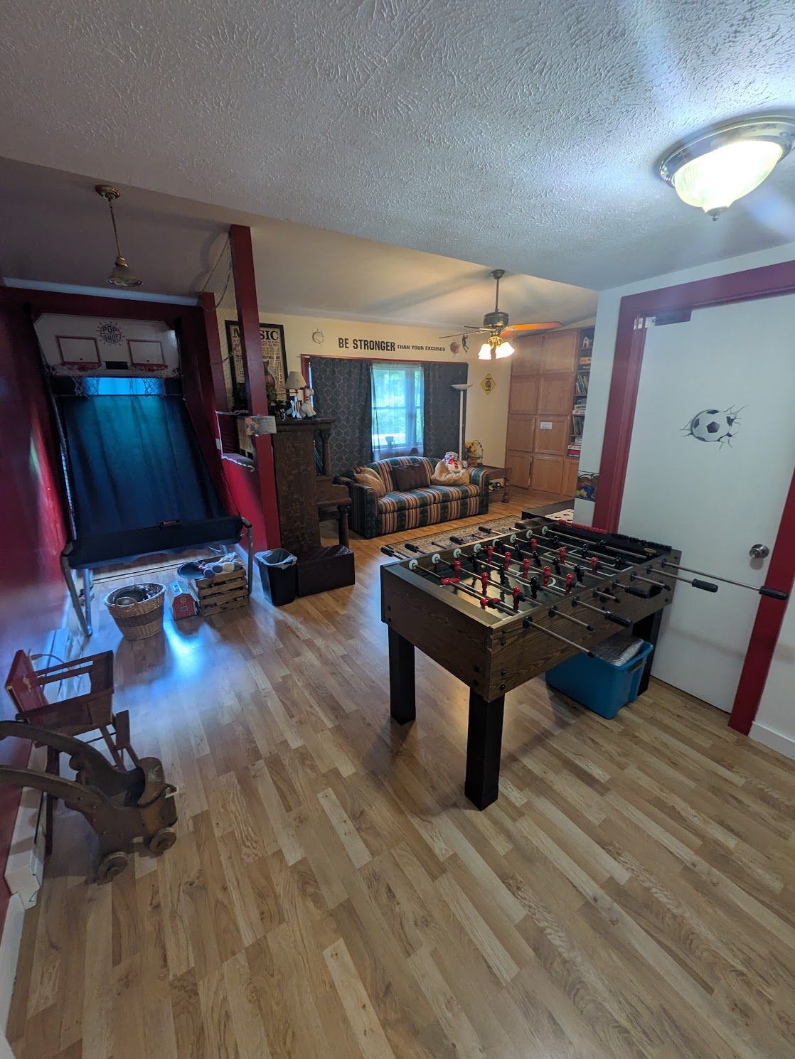 Cozy game room with foosball table, sofa, TV, red beams, and large windows