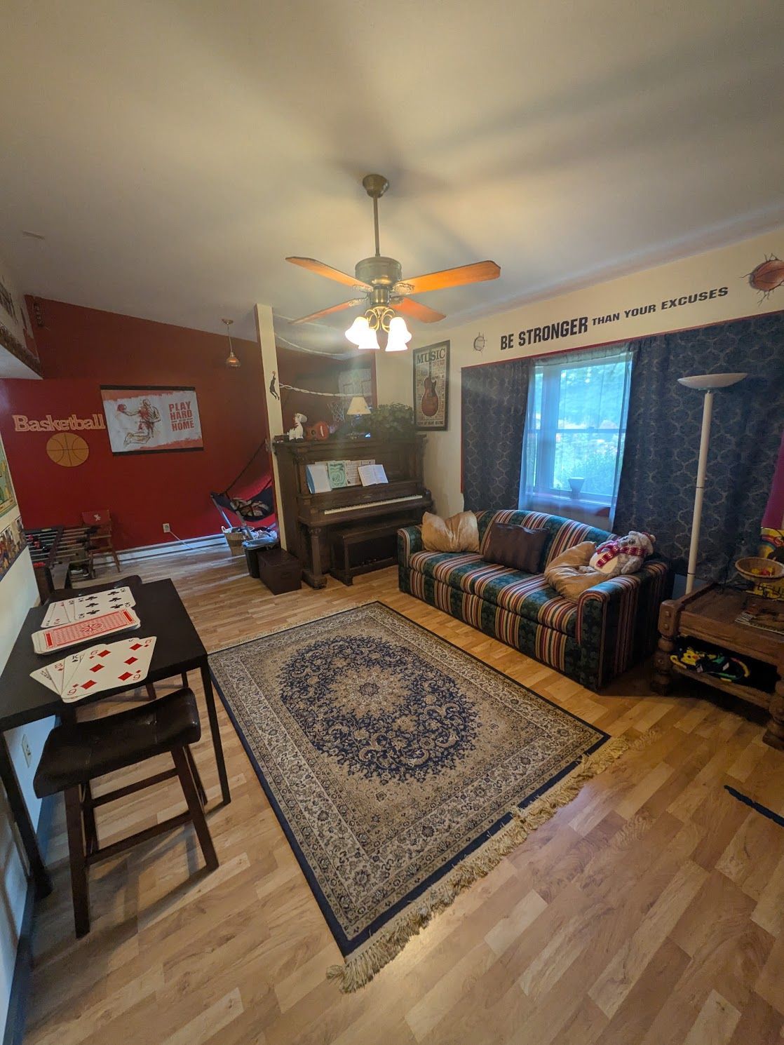 Cozy living room with red walls, patterned rug, couch, piano, and ceiling fan by a window.
