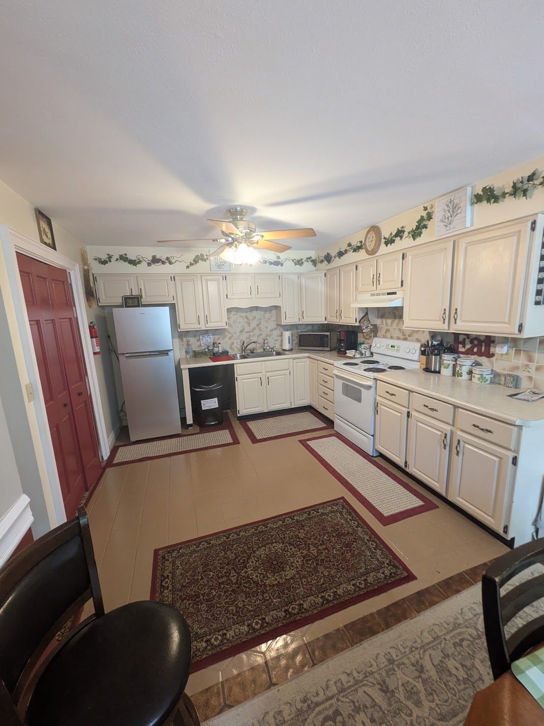 Bright kitchen with white cabinets, tiled floor, rugs, and a ceiling fan.