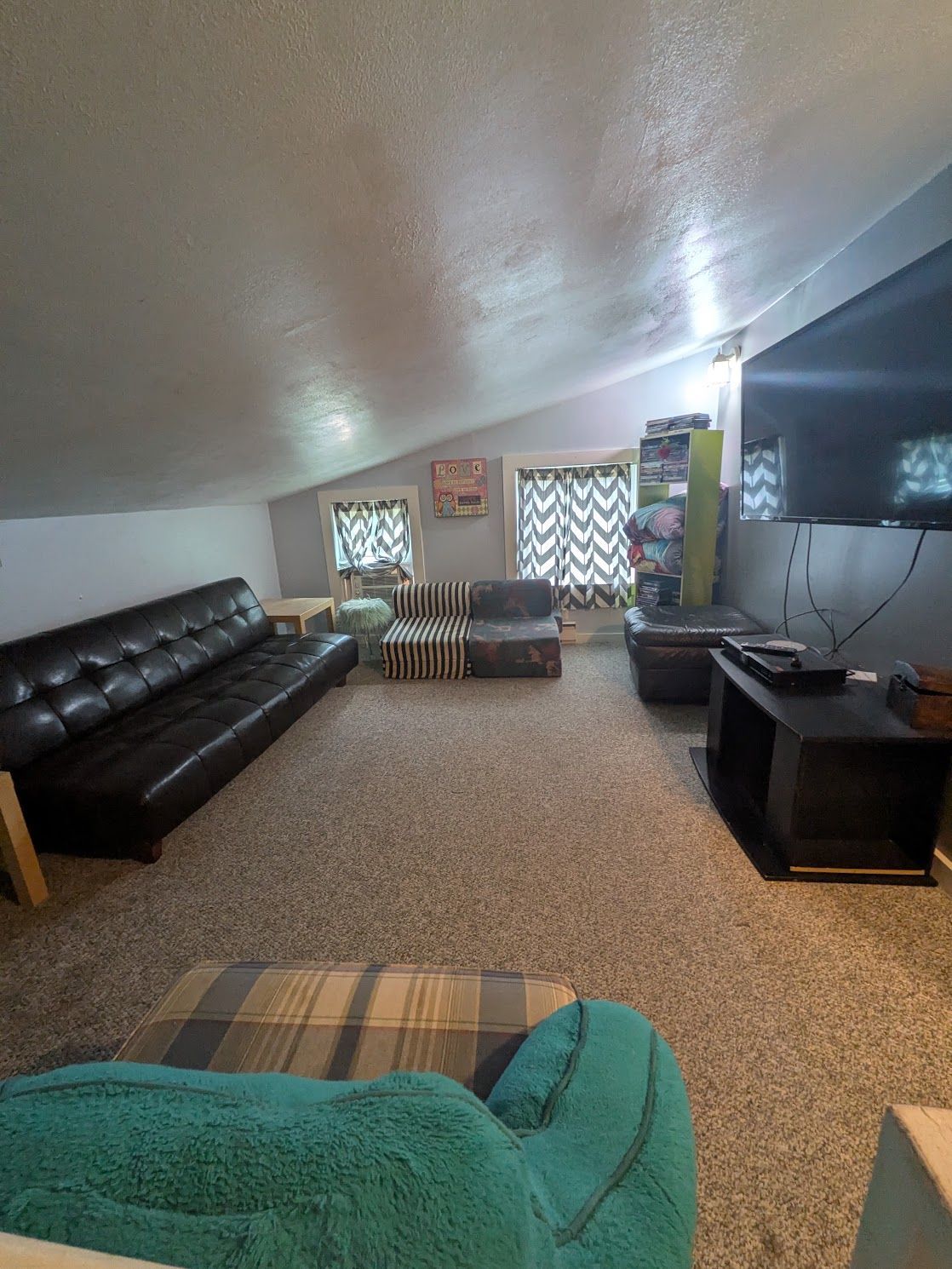 Living room with black leather sofa, TV stand, and patterned curtains under a slanted ceiling.