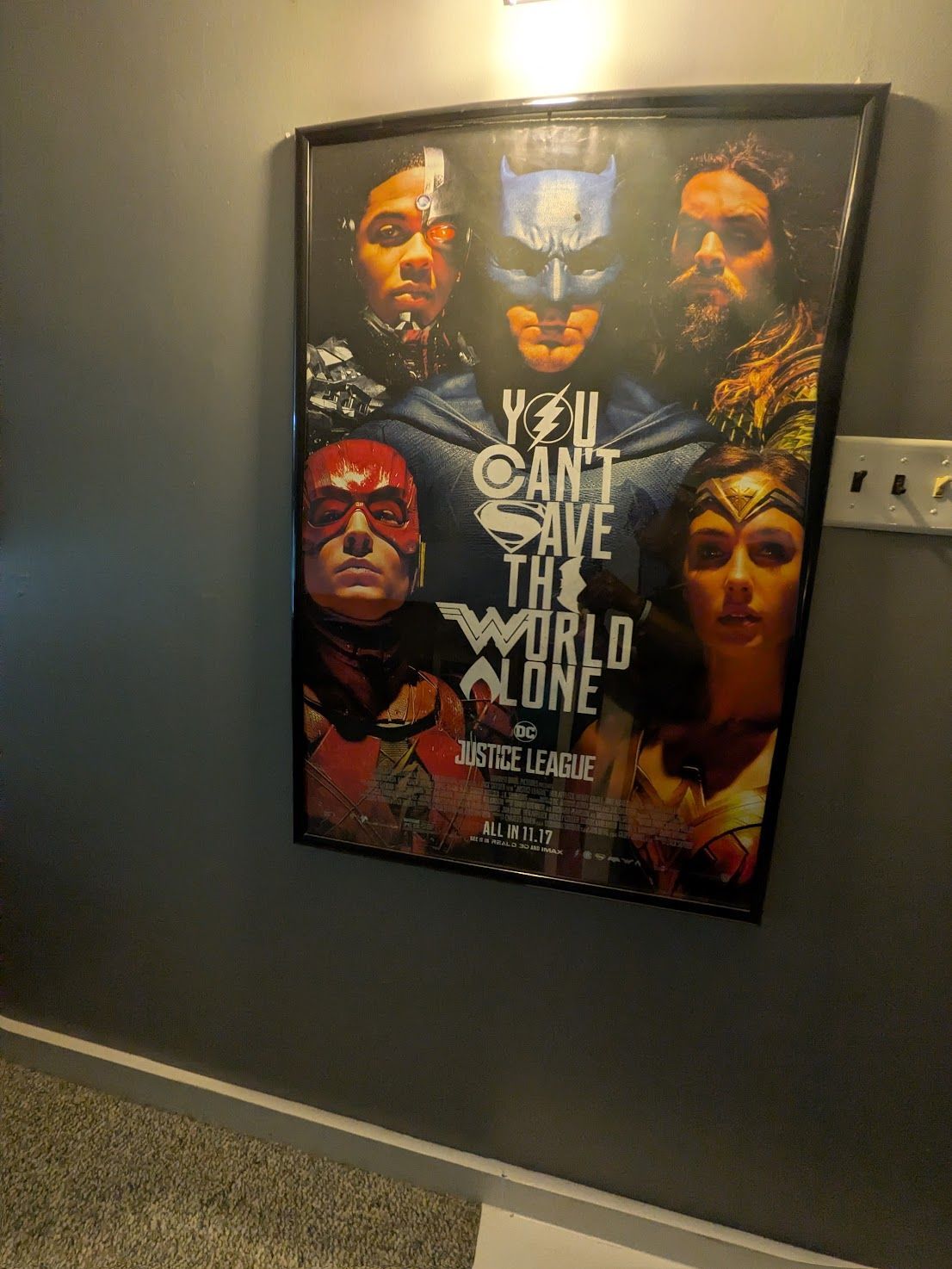 Framed Justice League poster on a gray hallway wall, with characters and the text “You can’t save the whole world.”