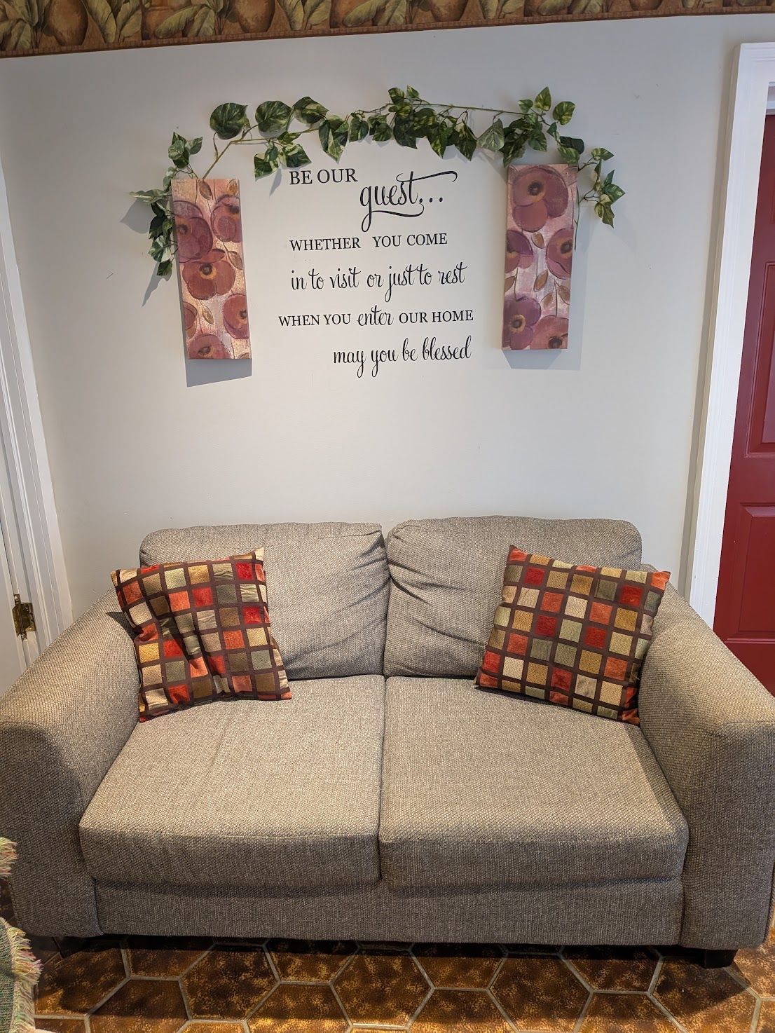 Cozy beige loveseat with patterned pillows beneath a floral wall sign in a home nook