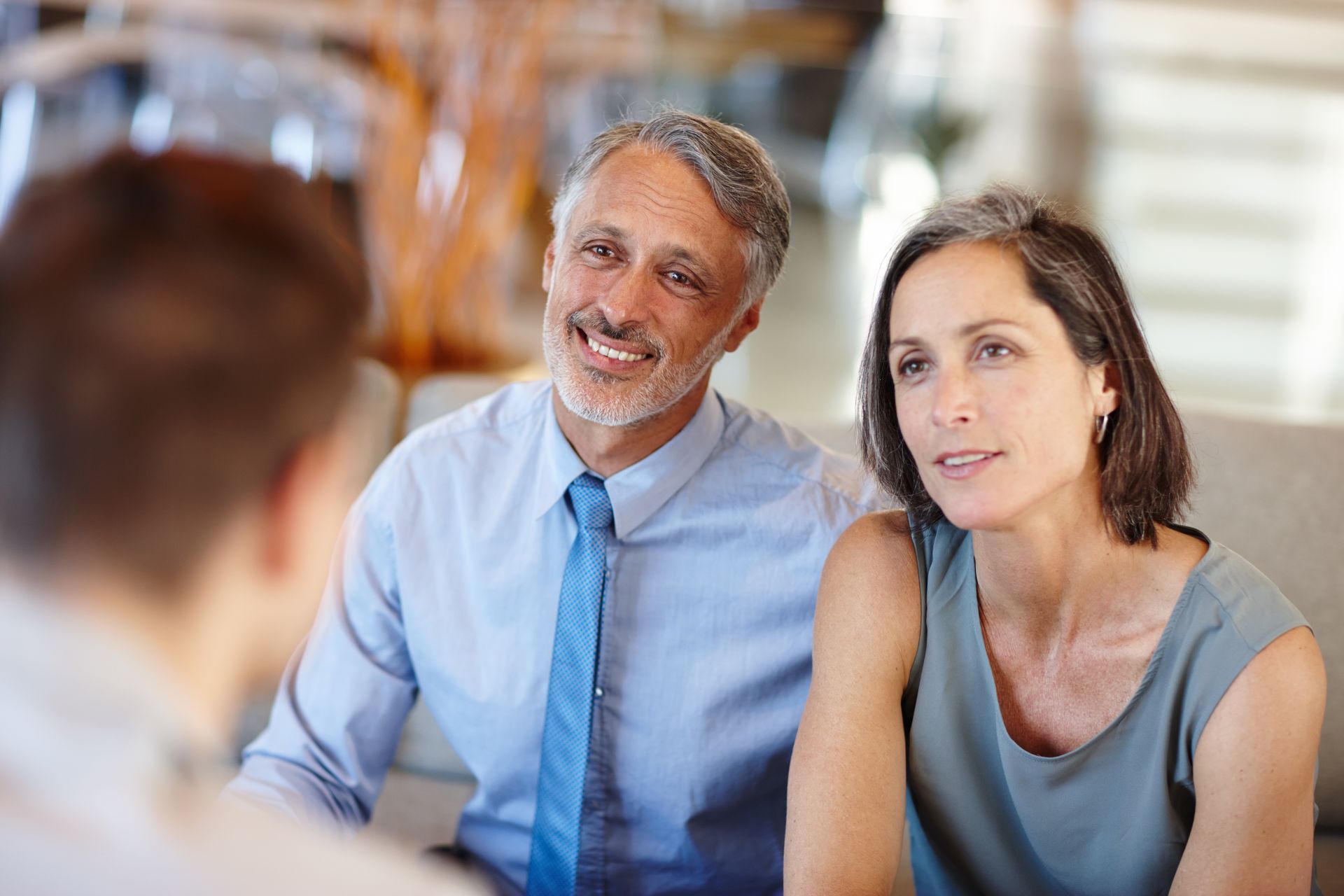 Two people smiling in a meeting, seated across from someone in the foreground.
