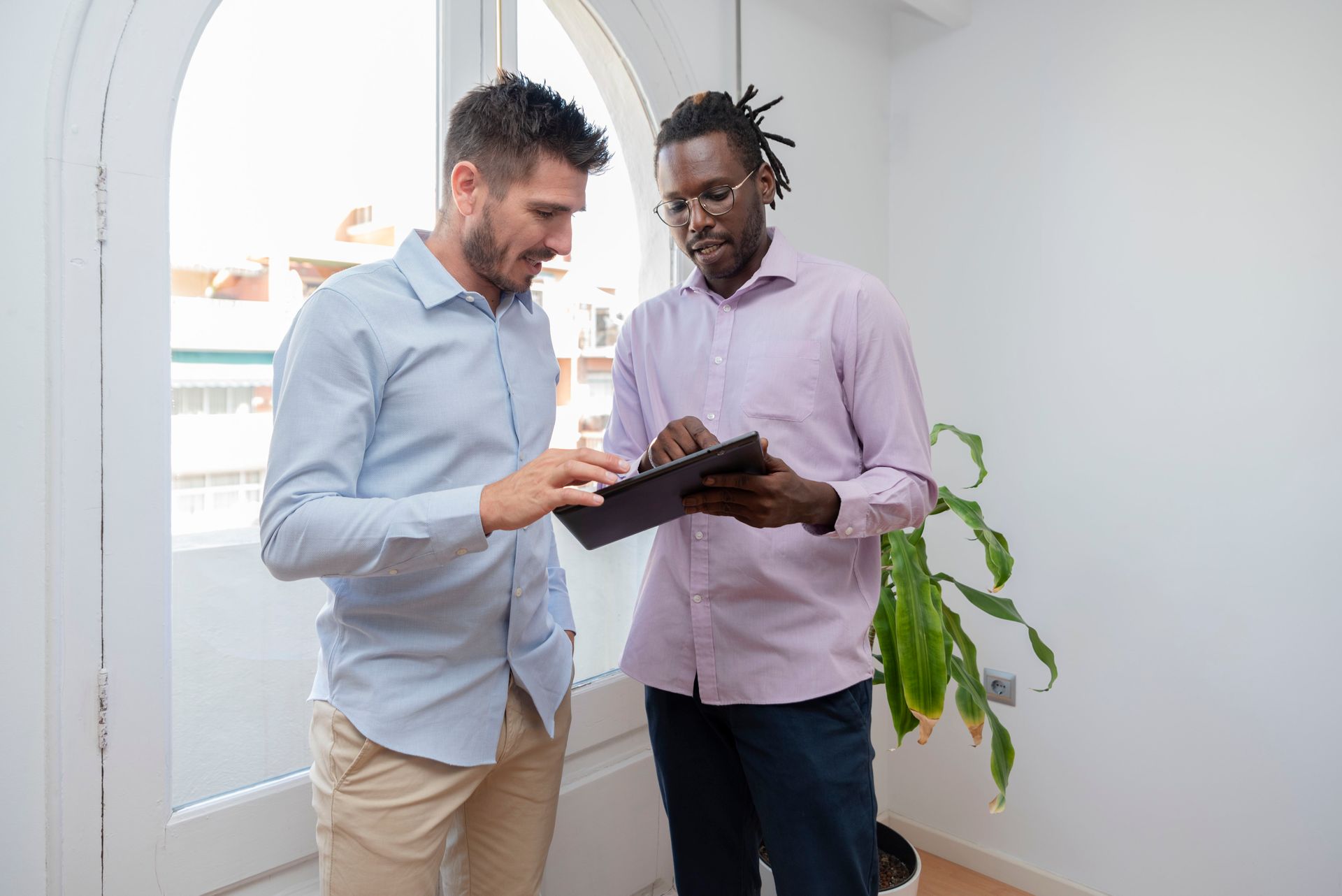 Two men reviewing a tablet together in a bright office hallway