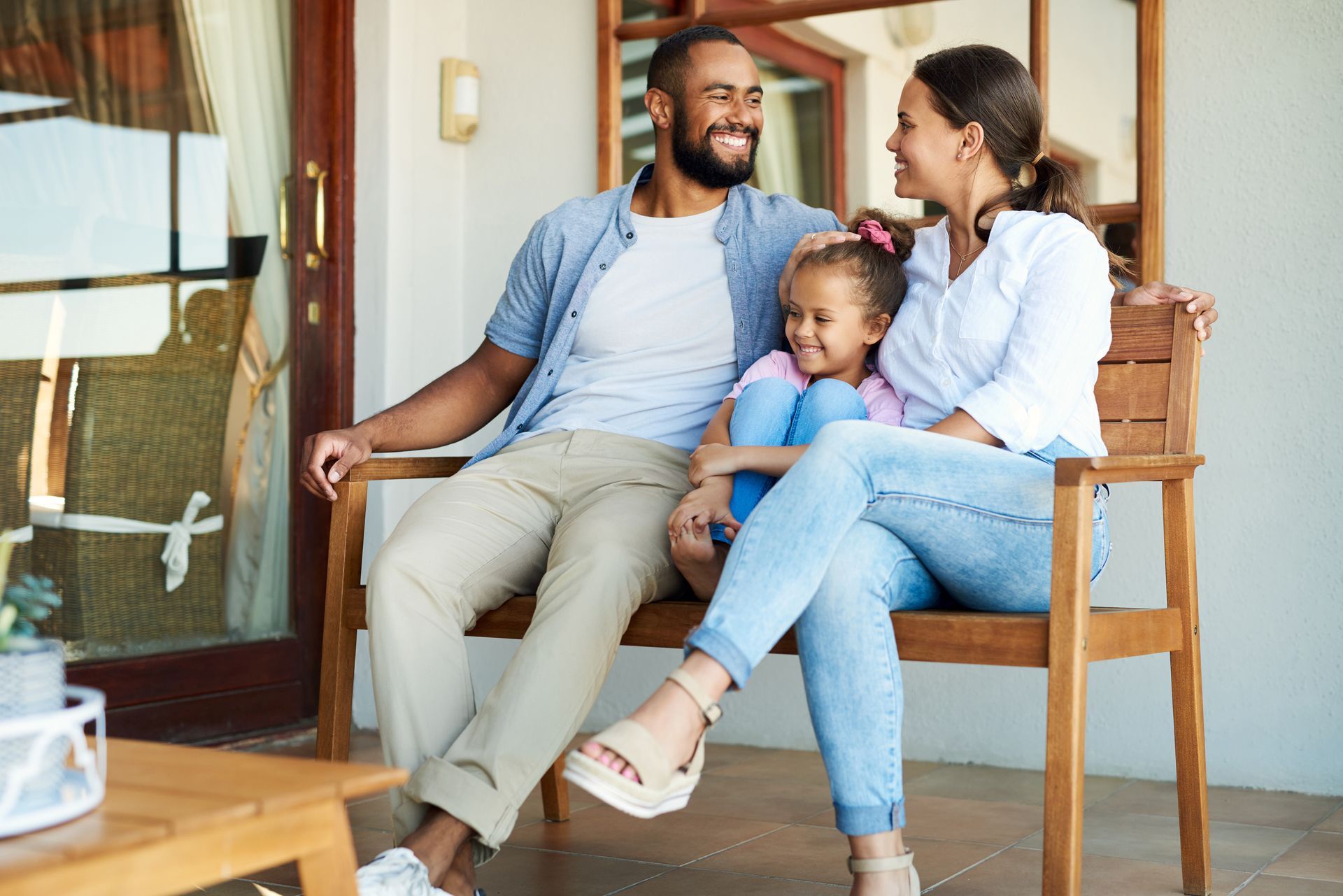 Family sitting on a porch bench, smiling and chatting in a cozy outdoor setting
