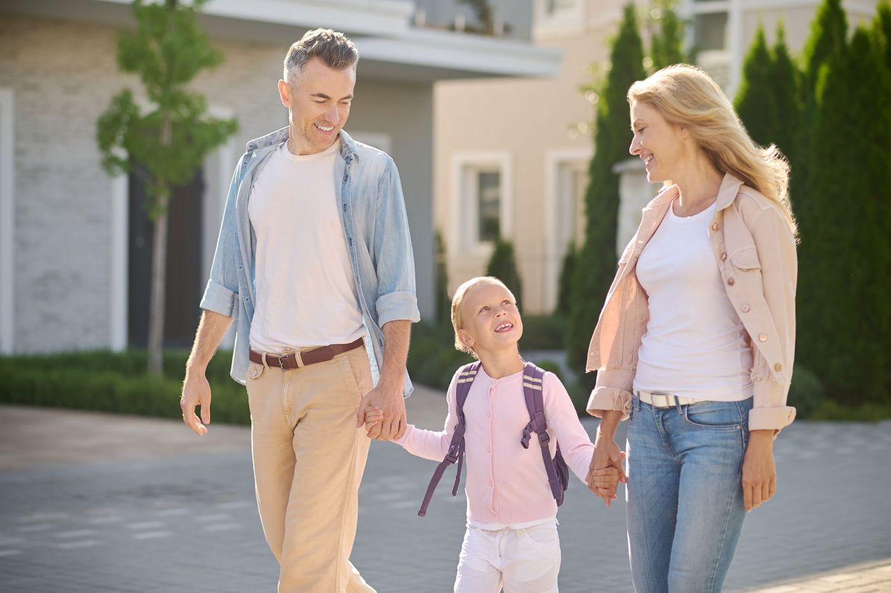 Three people walking together outdoors, smiling in a sunny suburban neighborhood