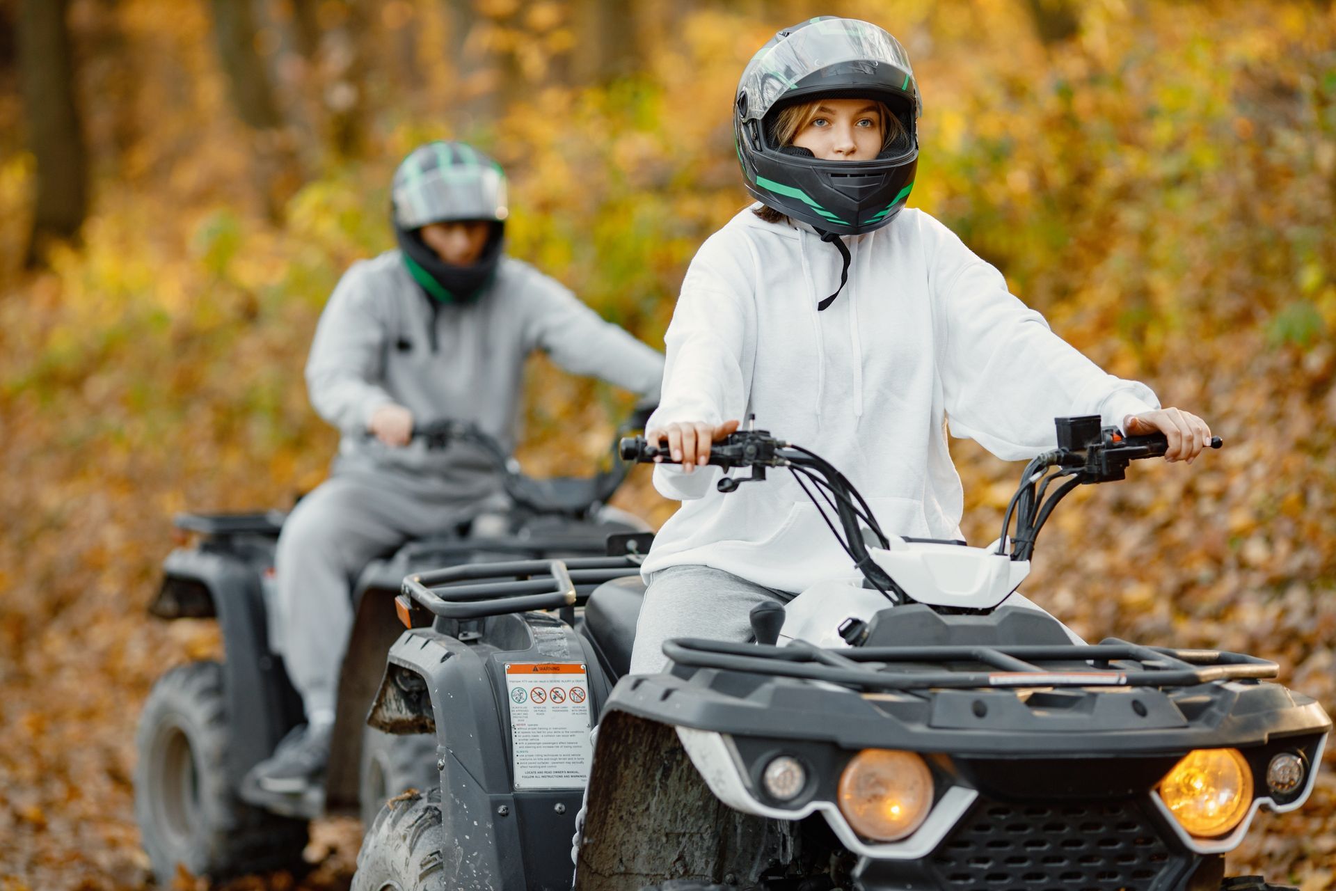 Two people riding ATVs on a dirt trail in helmets and riding gear