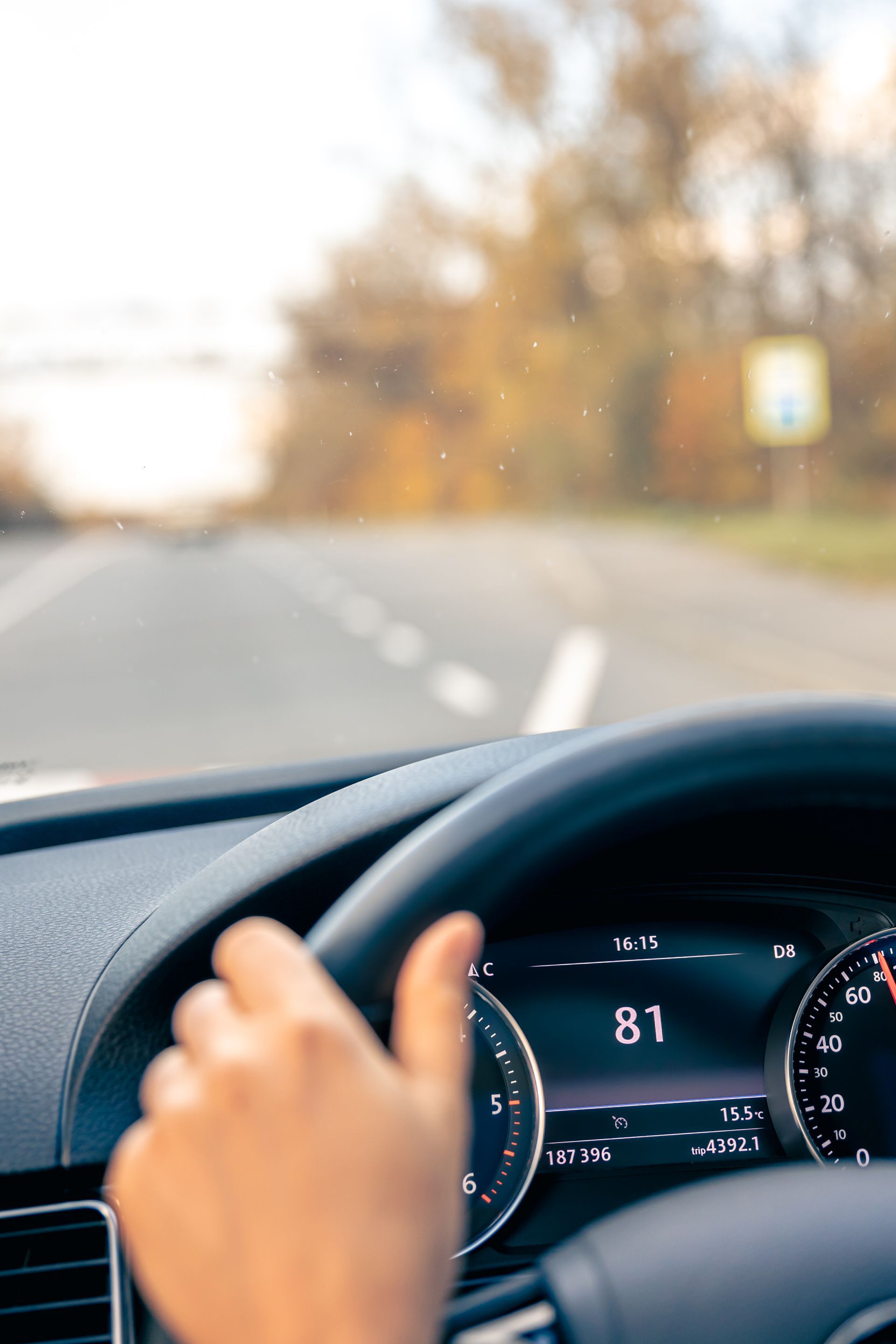 Hand on steering wheel, driving a car on a blurred road with dashboard speed reading 81