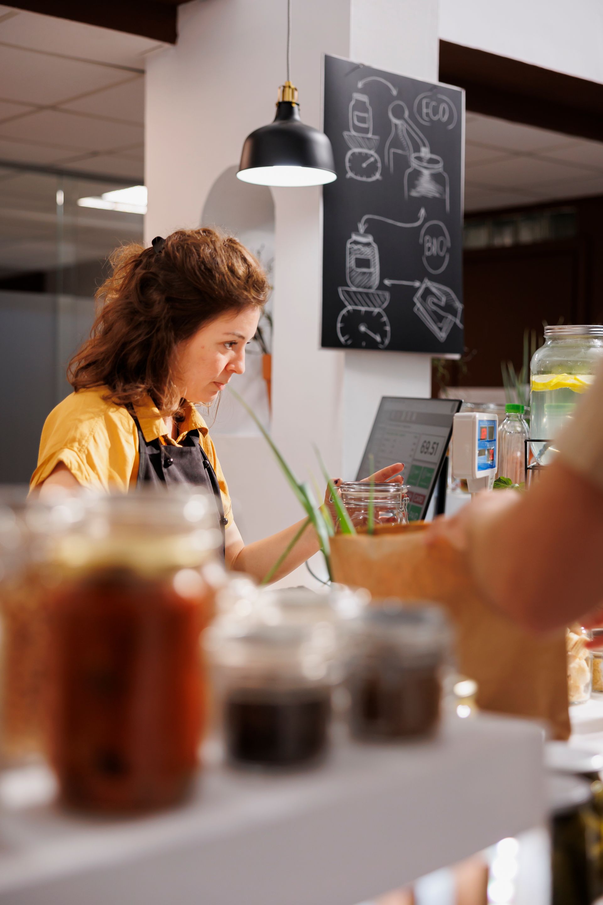 Barista serving coffee at a café counter beneath a chalkboard menu