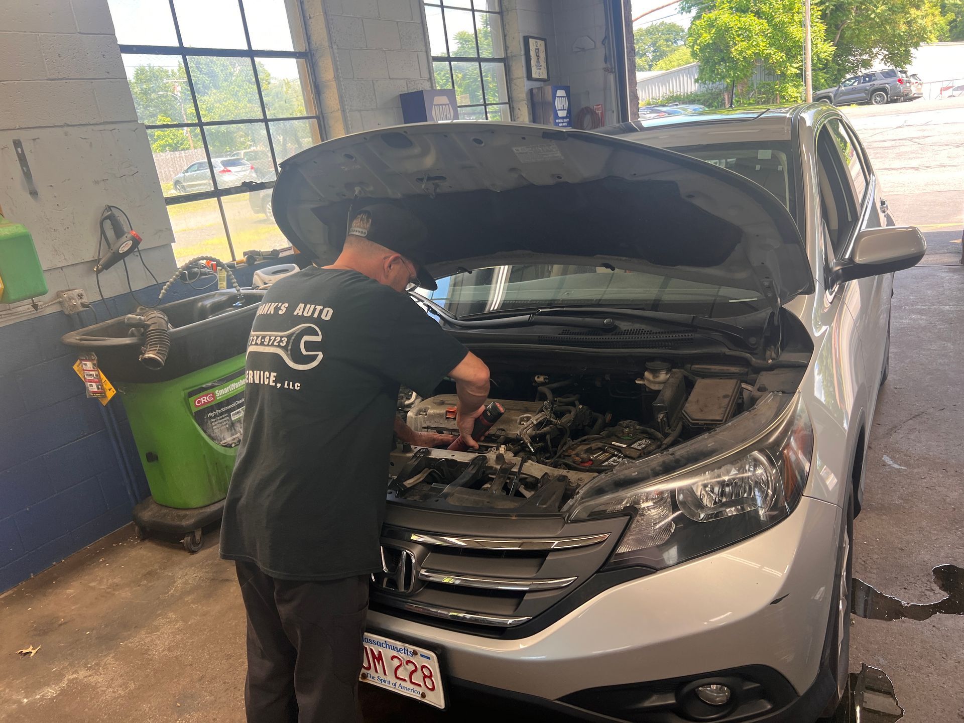 Mechanic working under open hood of silver car inside an auto repair shop
