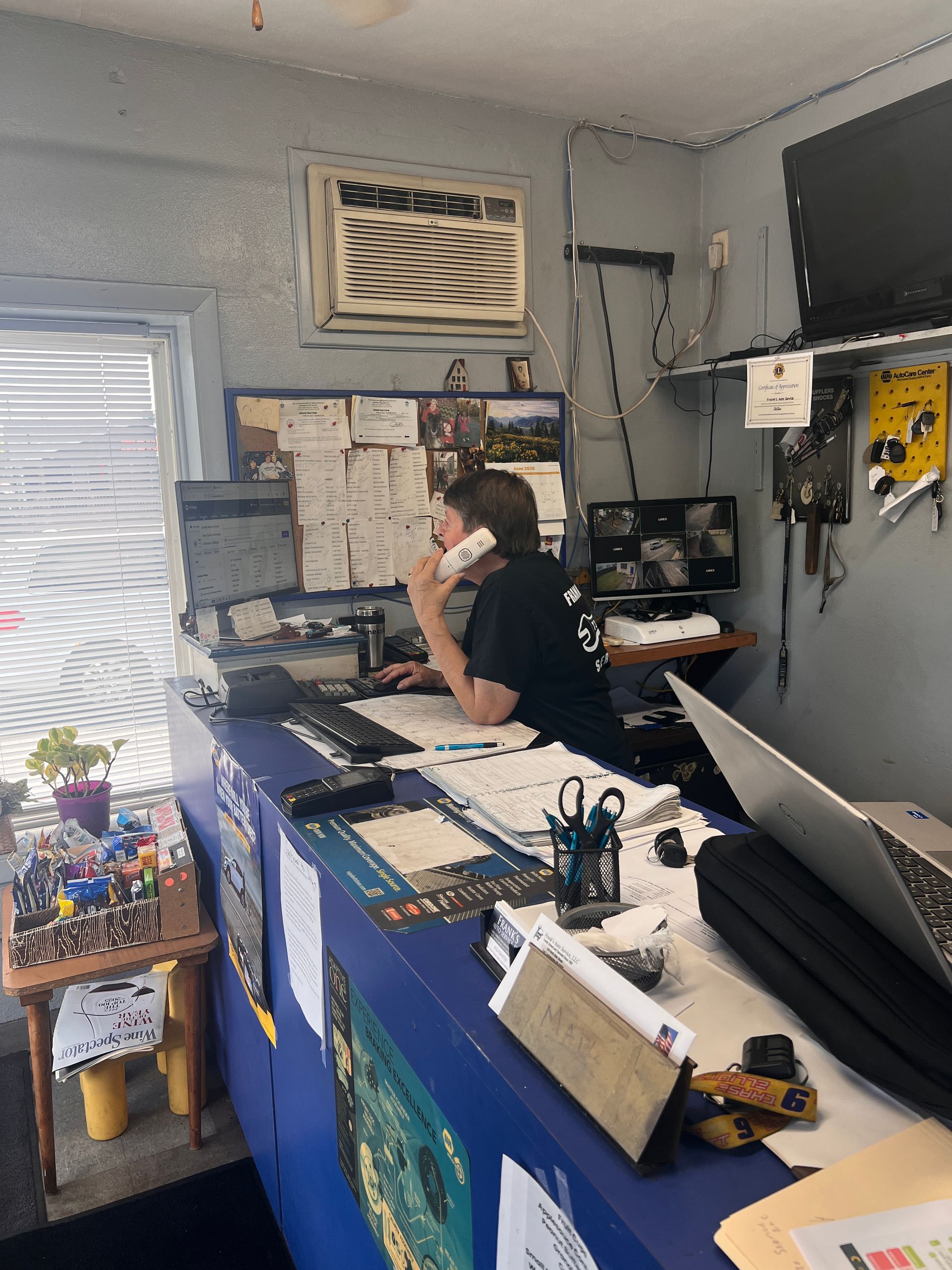 Person on phone at a cluttered office desk with blue drawers, papers, and computer equipment