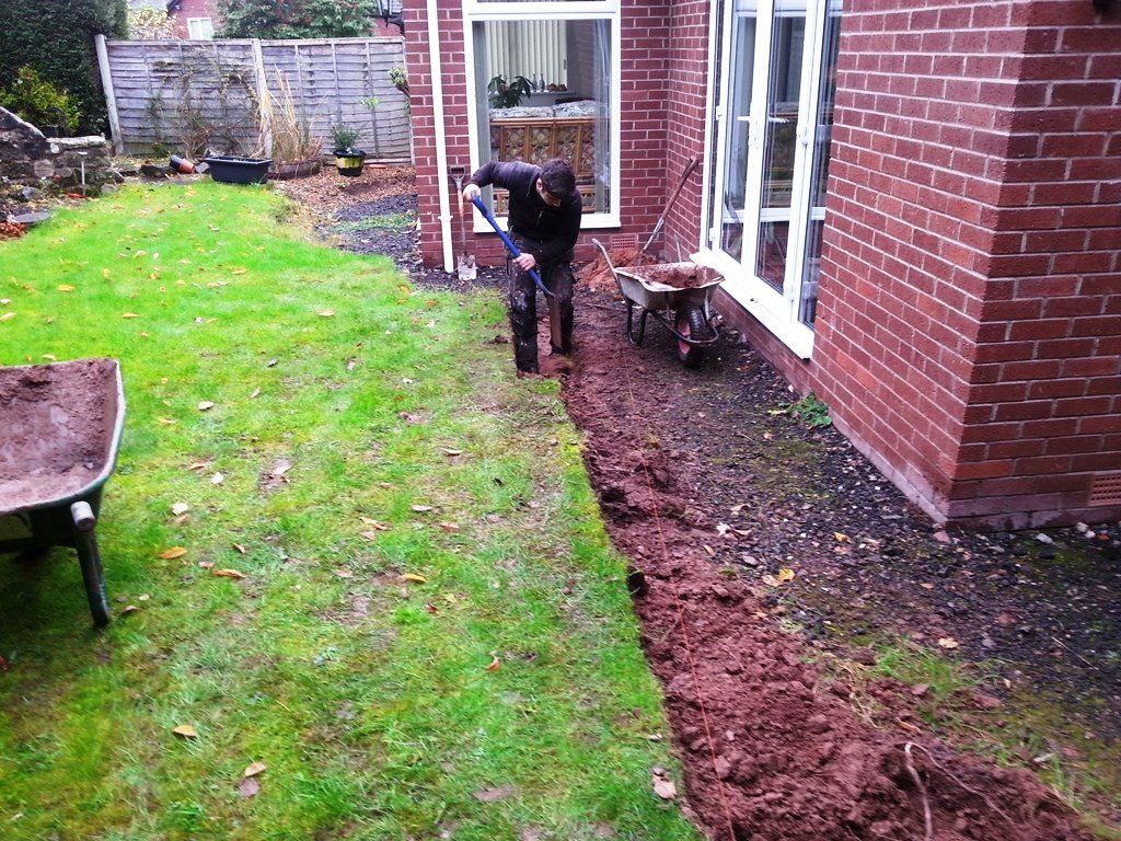 A man is digging in a yard next to a brick building.