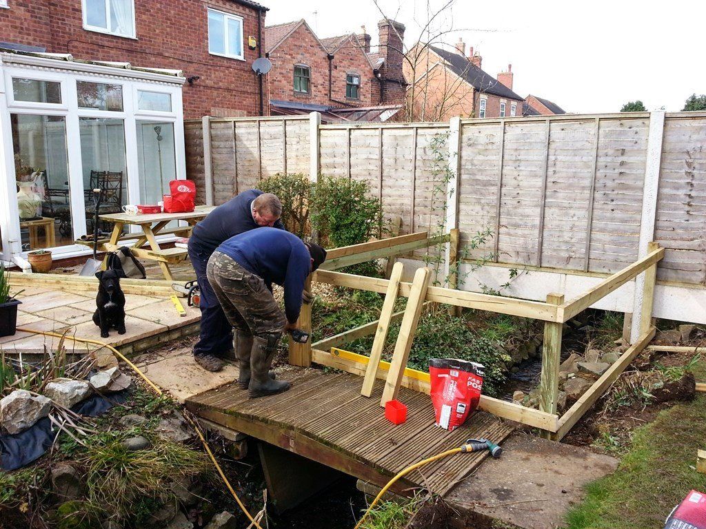 Two men are working on a wooden deck in a backyard.