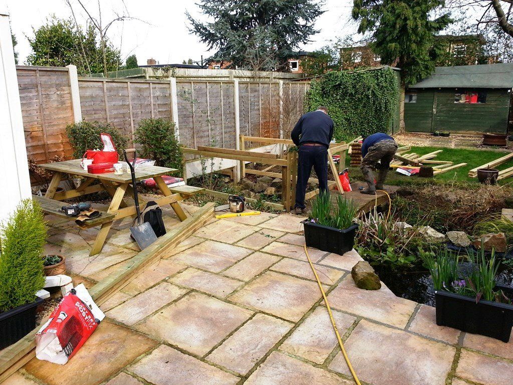 Two men are working on a patio in a garden.