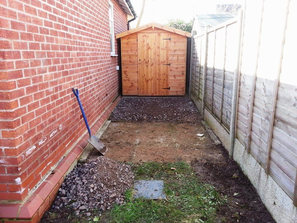 There is a wooden shed in the backyard next to a brick wall.