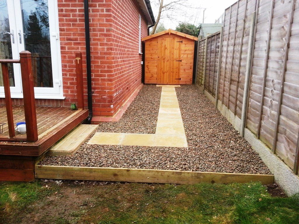 A brick house with a wooden shed and a gravel path leading to it.